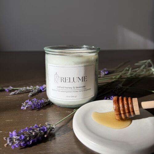 A 10-ounce Relume candle on a dark wood table. The candle is surrounded by lavender and honey.