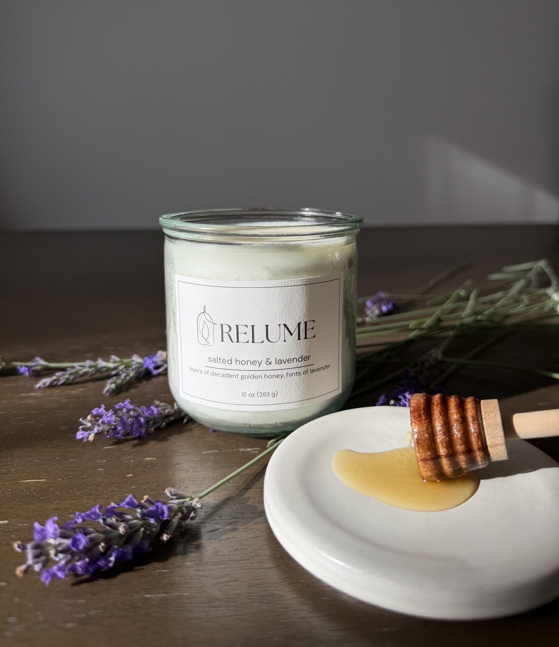 A 10-ounce Relume candle on a dark wood table. The candle is surrounded by lavender and honey.